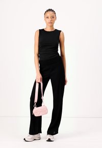 Haut noir sans manches avec détail froncé associé à un pantalon noir ample, tenant un petit sac à main rose. Portant des baskets avec des semelles légères.