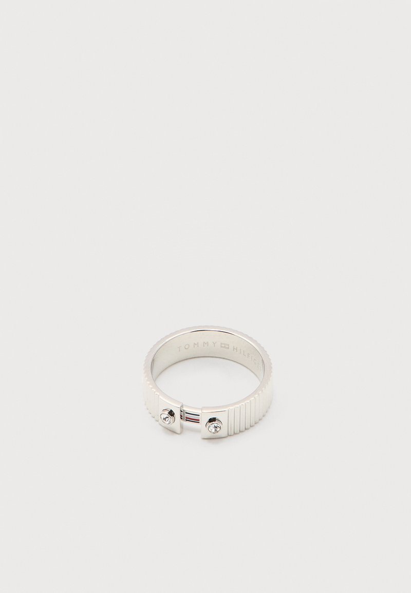 Bague Tommy Hilfiger ton argent avec bords striés, deux petits cristaux clairs près d'une ouverture, sur fond blanc uni.