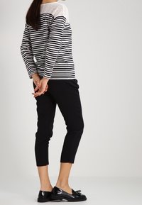 Mustat lyhyet housut, jotka on yhdistetty raidalliseen tummansiniseen ja valkoiseen paitaan, jossa on pitsiyksityiskohta. Mustat tasapohjaiset kengät viimeistelevät asun.