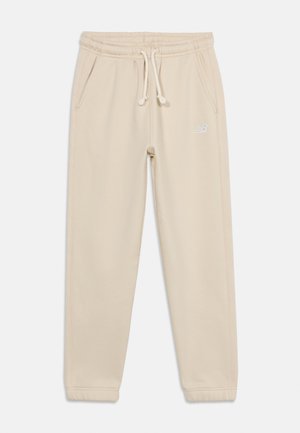 Μπεζ φόρμα με κορδόνι, ελαστική μέση και τελείωμα στα μανσέτα, πλαϊνές τσέπες και μικρό λευκό λογότυπο με γράμματα στο πάνω αριστερό μηρό.