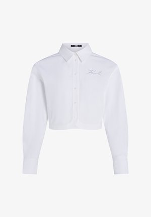 Bijela skraćena košulja s dugim rukavima, s klasičnim krojem i suptilno izvezenim logom na prsima. Glatka tekstura tkanine.