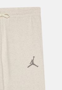 Pantalones de chándal de algodón gris claro con cinturilla elástica, cordón y un logo Jumpman bordado en gris en el muslo izquierdo.