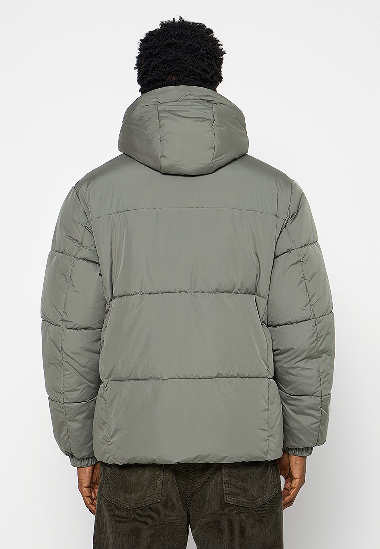 Chaqueta acolchada de color verde oliva con capucha, diseño acolchado y puños elásticos. Presenta una tela suave y resistente al agua.
