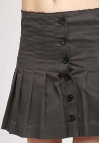Gonna grigia plissettata con vita alta, cinque bottoni neri sulla parte frontale e dettagli cuciti. Realizzata in tessuto leggero.