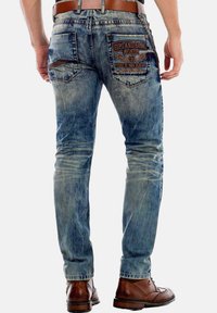 Slim-fit blauwe spijkerbroeken met een vervaagde was. Heeft gestikte zakken en een geborduurd logo op de achterzak. Bruin leren riem en schoenen.