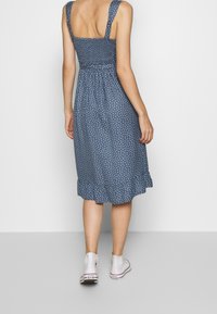 Vestido azul con lunares, con un corsé ajustado, tirantes anchos y un dobladillo acampanado, combinado con zapatillas deportivas blancas de caña alta.