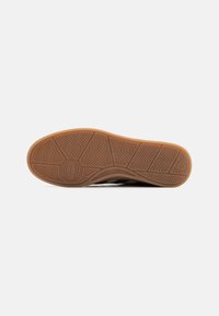Sole of a sneaker featuring a textured rubber surface in light brown with zigzag patterns and a circular logo detail.