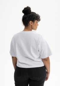 Witte, kortgebouwde T-shirt met ronde hals en een relaxte pasvorm, gecombineerd met zwarte high-waisted jeans. Gladde stof, minimaal ontwerp.