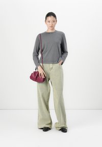 Woman wearing long-sleeve gray shirt, wide-leg light green jeans, black shoes, and holding a small burgundy crossbody bag against a white background.