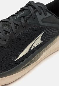 Chaussure de sport noire avec tige en maille, superpositions texturées et accents réfléchissants. Comprend des lacets plats et une semelle en caoutchouc. Modèle : Torin 8.