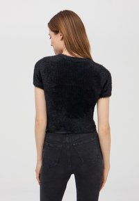 Maglione nero a maniche corte con una finitura morbida e testurizzata e un motivo a costine, abbinato a jeans scuri e aderenti con tasche posteriori.