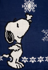 Coperta lavorata a maglia con Snoopy in bianco e nero su uno sfondo blu, decorata con fiocchi di neve bianchi e motivi lungo il bordo inferiore.