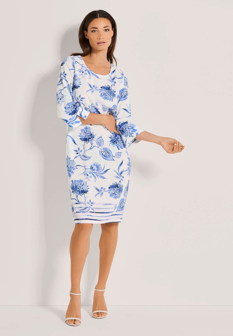 Weißes Blumenkleid mit blauen Mustern, dreiviertellangen Ärmeln, Rundhalsausschnitt und figurbetonter Passform, ergänzt durch einen gestreiften Saum und eine glatte Textur.