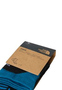 Czarne i turkusowe skarpetki trekkingowe do kostki, zapakowane z brązową tekturową etykietą, na której znajduje się logo i szczegóły produktu.