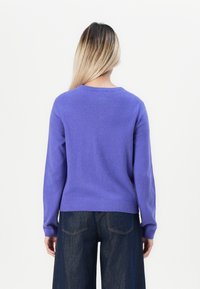 Un pull en tricot violet clair avec un col rond, des manches longues et des poignets côtelés. Associé à un pantalon large taille haute en jean bleu foncé.