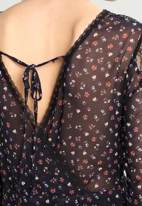 Schwarzes Kleid aus transparentem Stoff mit floralem Druck, mit einem tiefen Rücken und Spitzenbesatz sowie einem gebundenen Verschluss. Kurze Ärmel und zarte Akzente.