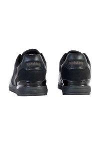 Des baskets noires avec une combinaison de cuir lisse et de tissu texturé, dotées d'une semelle rembourrée et du logo "Redskins" sur le talon.