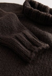 Maglione marrone scuro lavorato a maglia con texture a coste, collo alto ripiegato e maniche lunghe con polsini a coste. Materiale morbido e spesso.