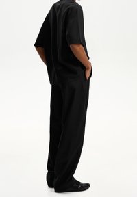 Černá košile s krátkým rukávem a široké kalhoty z lehké tkaniny, s volným střihem a skrytými bočními kapsami.