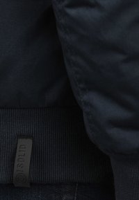 Veste marine avec un ourlet côtelé et un tissu lisse. Étiquette noire visible avec l'inscription « SOLID ». Pas de motifs ; design simple et classique.
