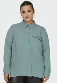 Light blue long-sleeve shirt with a button-down collar, textured fabric, single chest pocket, and buttoned cuffs.