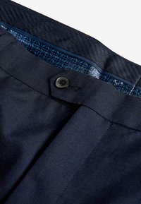 Marineblaue Hosen aus strukturiertem Stoff mit einem schwarzen Knopfverschluss und einem gefütterten Innenfutter mit geometrischen Mustern.