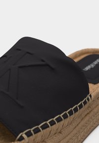 Μαύρο σανδάλι espadrille με εύκολη εφαρμογή, με πλεγμένη σόλα από ζαχαροκάλαμο και ανάγλυφο λογότυπο "CK" στο υφασμάτινο επάνω μέρος.