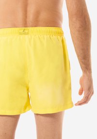 Gelbe Badehosen mit elastischem Bund, glatter Textur und Seitentasche. Das Design zeichnet sich durch minimalistische Details und eine lässige Passform aus.