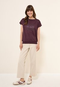 Lilla afslappet T-shirt med en struktureret mønster og "GRATEFUL MIND" trykt i hvid, parret med beige bredbenede bukser og sneakers.