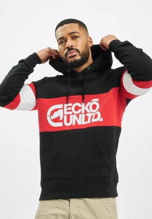 Zwarte en rode hoodie met witte details, groot logo aan de voorkant, koordjes in de capuchon en een kangoeroe-pocket. Heeft een color-blocked ontwerp.