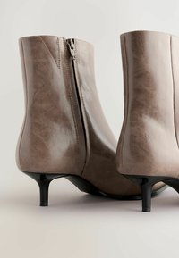 Bottines en simili cuir marron avec une texture lisse, fermeture éclair sur le côté et un petit talon noir. Présente un design élégant et ajusté.