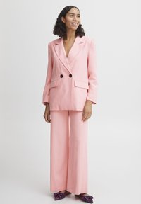 Rosa blazer med dobbeltradet design og sorte knapper, parret med bredbenede rosa bukser. Glat stof med en struktureret pasform.