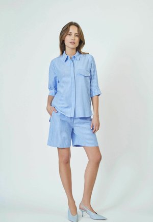 Blue and white striped short-sleeve shirt with chest pocket, paired with matching striped shorts. Model wears light blue heels.