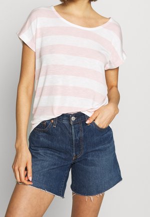 Persoon draagt een roze-wit gestreept shirt met korte mouwen, ingestopt in een hooggetailleerde donkere denimshorts met rafelige zoom.