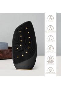 Svart silikonansiktsrengöringsapparat med gulddetaljer, strukturerad yta, ergonomisk form och vattentålig design. Har knappar på basen.