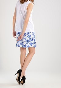 Biała bezrękawnikowa bluzka w zestawieniu z niebieską i białą spódnicą w kwiatowy wzór. Czarne szpilki dopełniają całość.