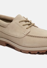 Scarpe in suede beige con cuciture in rilievo e lacci tondi. Suola in gomma spessa e testurizzata di un tono marrone chiaro.