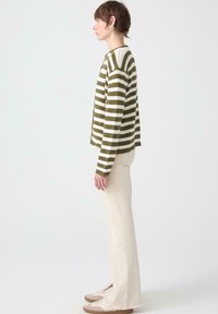 Grön- och vitrandig stickad tröja, rund halsringning, bärs med krämfärgade utsvängda byxor och beige sneakers, vilket visar en avslappnad silhuett.
