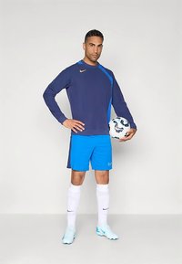 Nike edzőfelszerelés sötétkék hosszú ujjú felsővel, kék részletekkel, élénk kék rövidnadrággal, fehér zoknival és világoskék focicipővel.