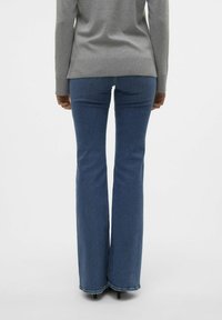 Jean bleu évasé en denim, doté d'une taille haute et d'un ourlet propre. Associé à un haut gris à manches longues.