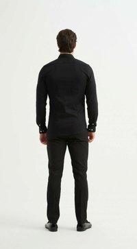 Chemise noire à manches longues avec des poignets boutonnés, design ajusté, texture lisse, assortie à un pantalon noir et des chaussures noires.