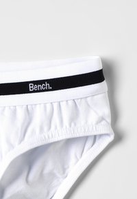 Witte katoenen slips met elastische tailleband, voorzien van een zwarte streep en witte tekst met daarop "Bench." Textuurstof met geplooide zijkanten.