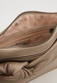 Beige Lederclutch mit Knotendetail, Reißverschluss und weichem Innenfutter. Verfügt über mehrere Fächer zur Organisation.