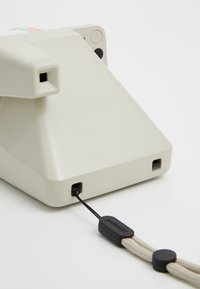 Appareil photo Polaroid en plastique blanc cassé au design minimaliste. Il est équipé d'un cordon noir avec un onglet pour une prise en main facile et d'une prise en main texturée.