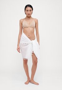 Bikini-set med en stripete beige halterneck-top og en hvit, teksturert sarong med duskdetaljer, som er drapert rundt livet.