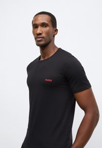 Černé bavlněné tričko s kulatým výstřihem a krátkými rukávy, s malým červeným logem "HUGO" na levé straně hrudi.