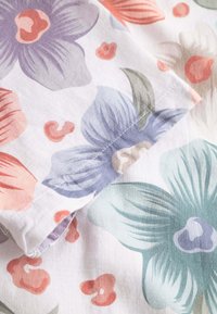 Tessuto di cotone floreale con fiori viola, corallo e verdi su uno sfondo bianco, con dettagli di cucitura visibili lungo il bordo.