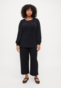 Black top with textured body and long, puffed sleeves. Paired with black wide-leg trousers and flat black shoes. Simple, elegant design.