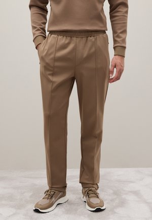 Pantalones marrones de cintura elástica con bolsillos laterales, diseño tapered y textura suave, combinados con zapatillas a juego en marrón y gris.