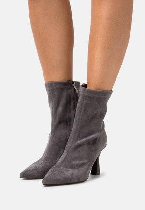 Botines de ante gris con punta afilada, tacón alto y textura suave. Incluyen una cremallera lateral para un fácil uso.